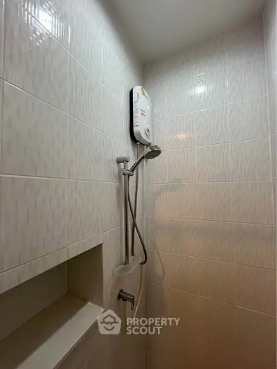 Compact bathroom shower area with modern water heater and tiled walls.