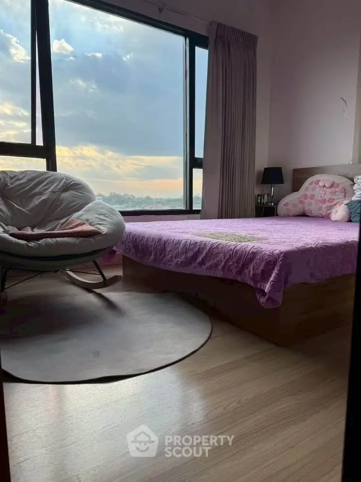 Cozy bedroom with large window offering stunning city view and comfortable seating.