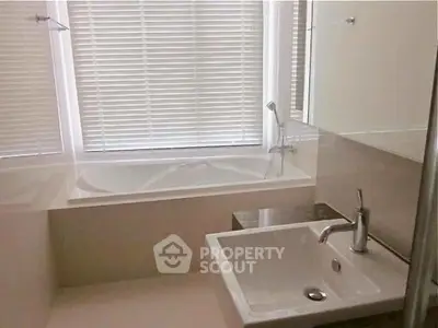 Modern bathroom with sleek sink and bathtub, featuring elegant blinds for privacy.
