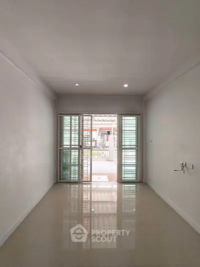 Spacious empty room with glossy tiled floor and large sliding glass doors leading to a patio.