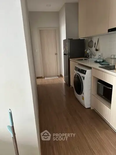 Modern kitchen with wooden flooring, washing machine, and sleek cabinetry.