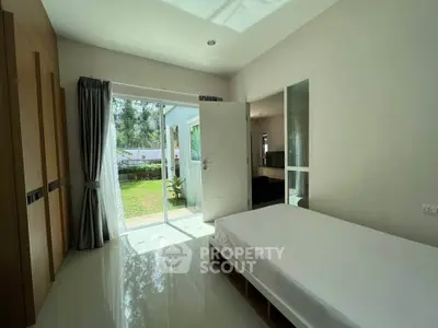 Bright bedroom with large windows opening to a lush garden view, featuring sleek modern design and ample natural light.