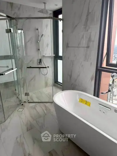 Luxurious bathroom with marble tiles, glass shower, and freestanding bathtub offering city views.