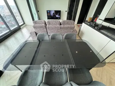 Modern living room with glass dining table and plush seating, offering stunning city views from high-rise apartment.