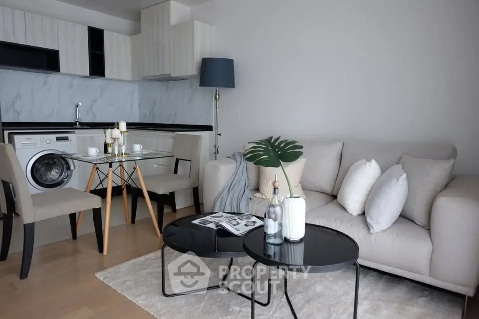 Modern living room with open kitchen, featuring stylish furniture and a washing machine.