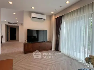 Spacious living room with modern decor and large TV, featuring elegant curtains and natural light.