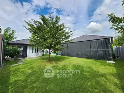 Spacious garden with modern house and lush greenery under blue sky.