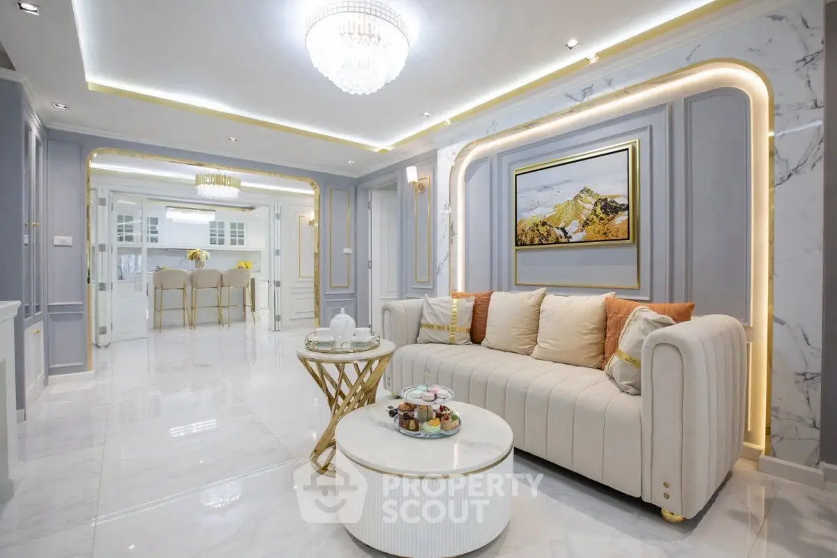 Luxurious living room with elegant decor and open layout leading to dining area, featuring plush sofa and chandelier.