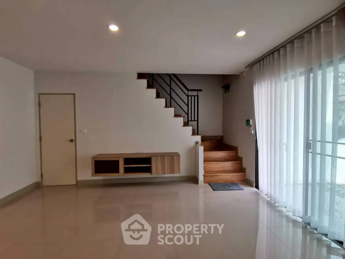 Spacious modern living room with staircase and large window for natural light.