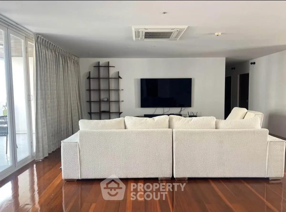 Spacious modern living room with sleek white sofa and large TV, perfect for relaxation.