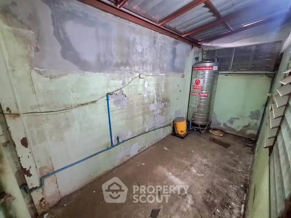 Industrial storage room with water tank and exposed pipes, ideal for utility use.