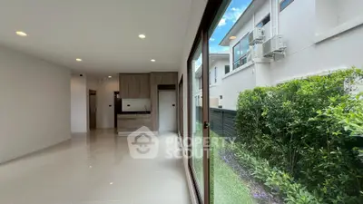Modern open-plan living room with garden view and sleek kitchen design.