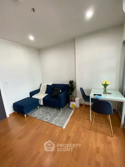 Modern living room with blue sofa and dining area, featuring wooden flooring and bright lighting.