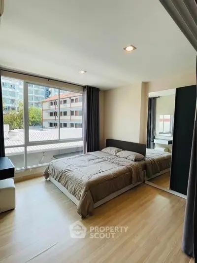 Modern bedroom with large window and mirrored wardrobe in urban apartment