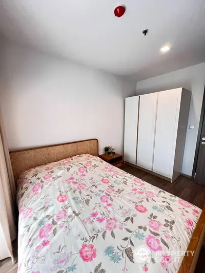 Cozy bedroom with a large bed adorned with floral bedding, ample storage with a white wardrobe, and warm wooden flooring.