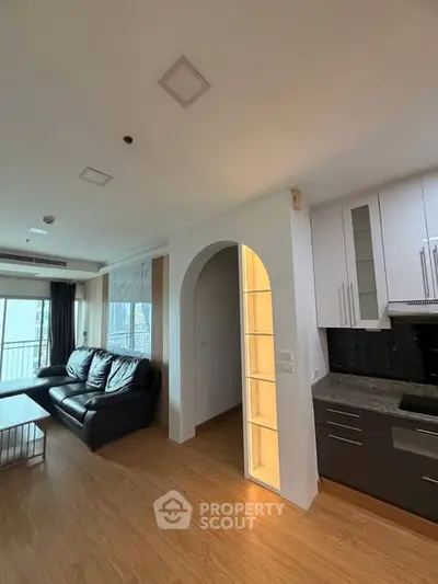 Modern living room with open kitchen and stylish archway, featuring sleek black and white cabinetry.