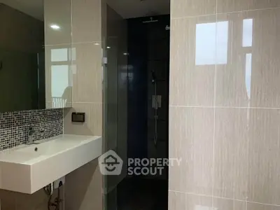 Modern bathroom with sleek sink and glass shower enclosure in contemporary apartment.