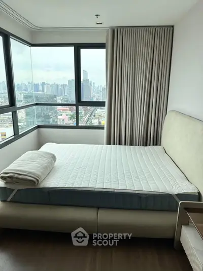 Spacious bedroom with panoramic city view and modern furnishings in high-rise apartment.