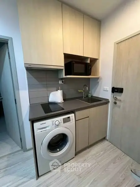Compact modern kitchen with washing machine and microwave in a cozy apartment.