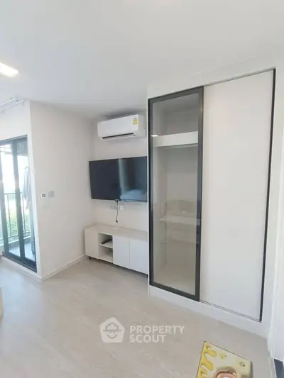 Modern living room with sleek TV setup and sliding closet doors in a bright apartment.