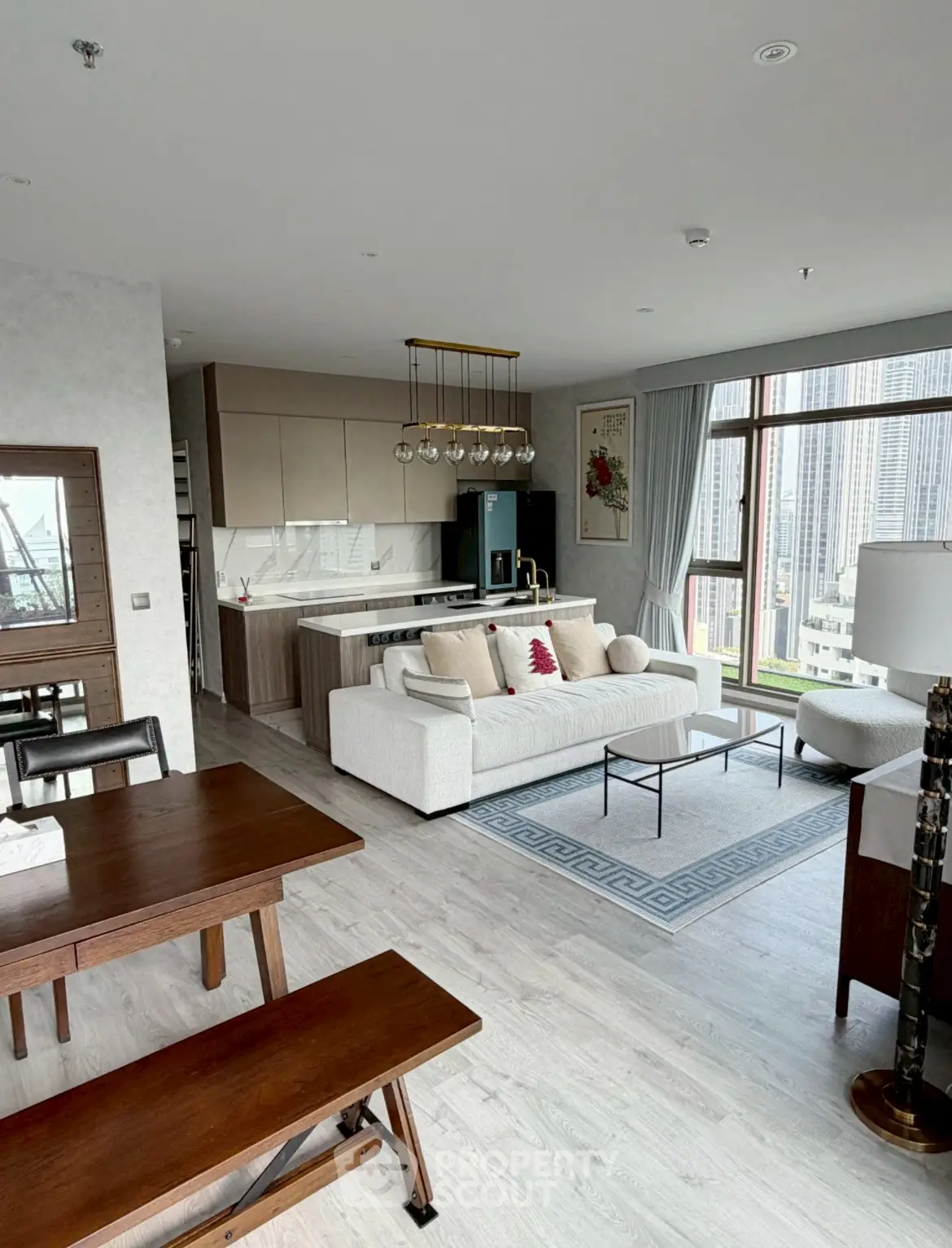 Spacious modern living room with open kitchen and city view, featuring elegant decor and natural light.