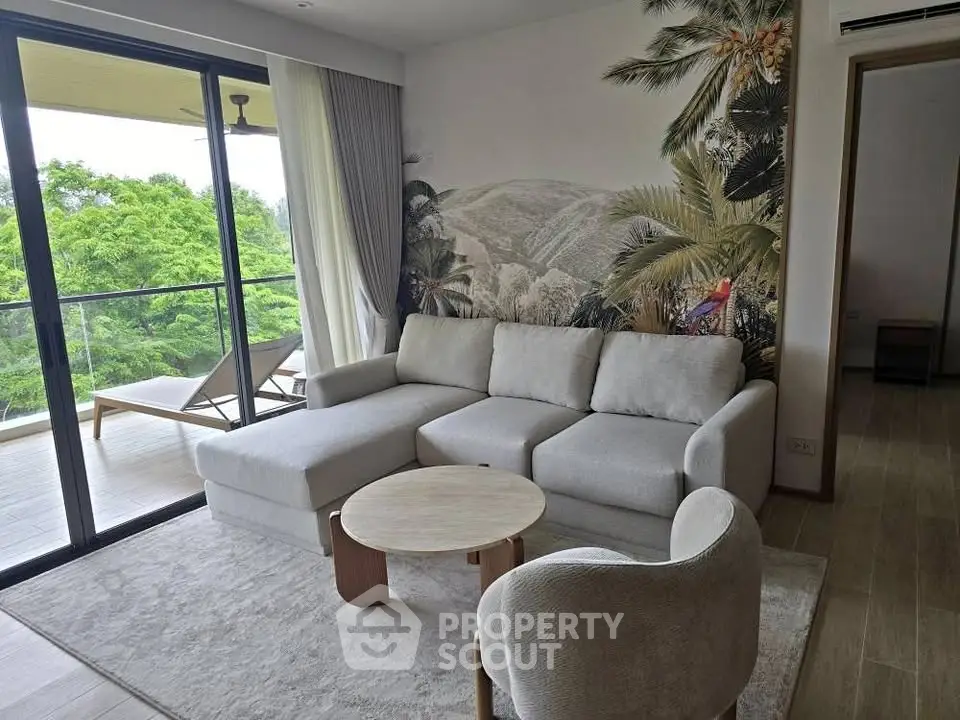 Stylish living room with modern sofa, tropical mural, and balcony view in a luxurious apartment.