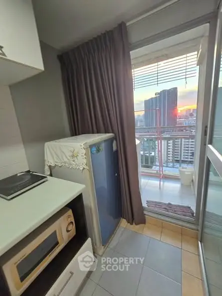 Compact kitchen with microwave and fridge, leading to a balcony with stunning city view at sunset.