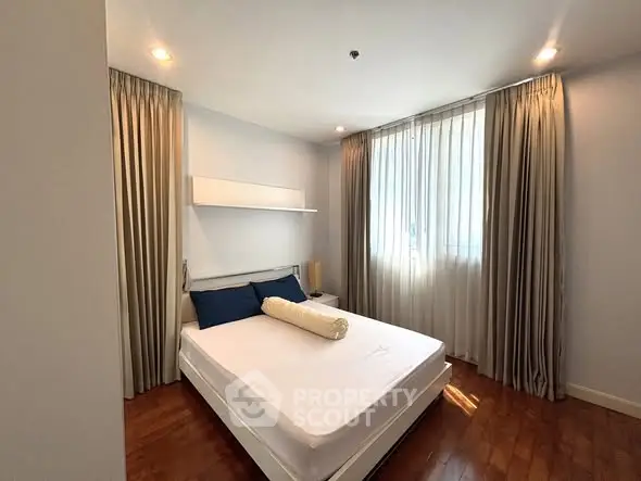 Cozy bedroom with elegant curtains and wooden flooring, perfect for relaxation.