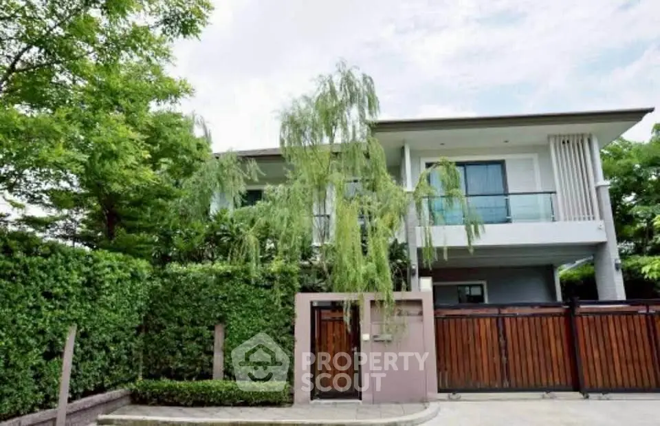 Modern two-story house with lush greenery and wooden gate in a serene neighborhood.