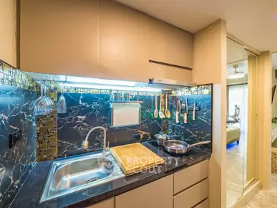 Modern kitchen with sleek design and marble backsplash, featuring stainless steel sink and utensils.