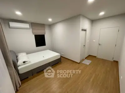 Spacious minimalist bedroom with wooden flooring and modern air conditioning.