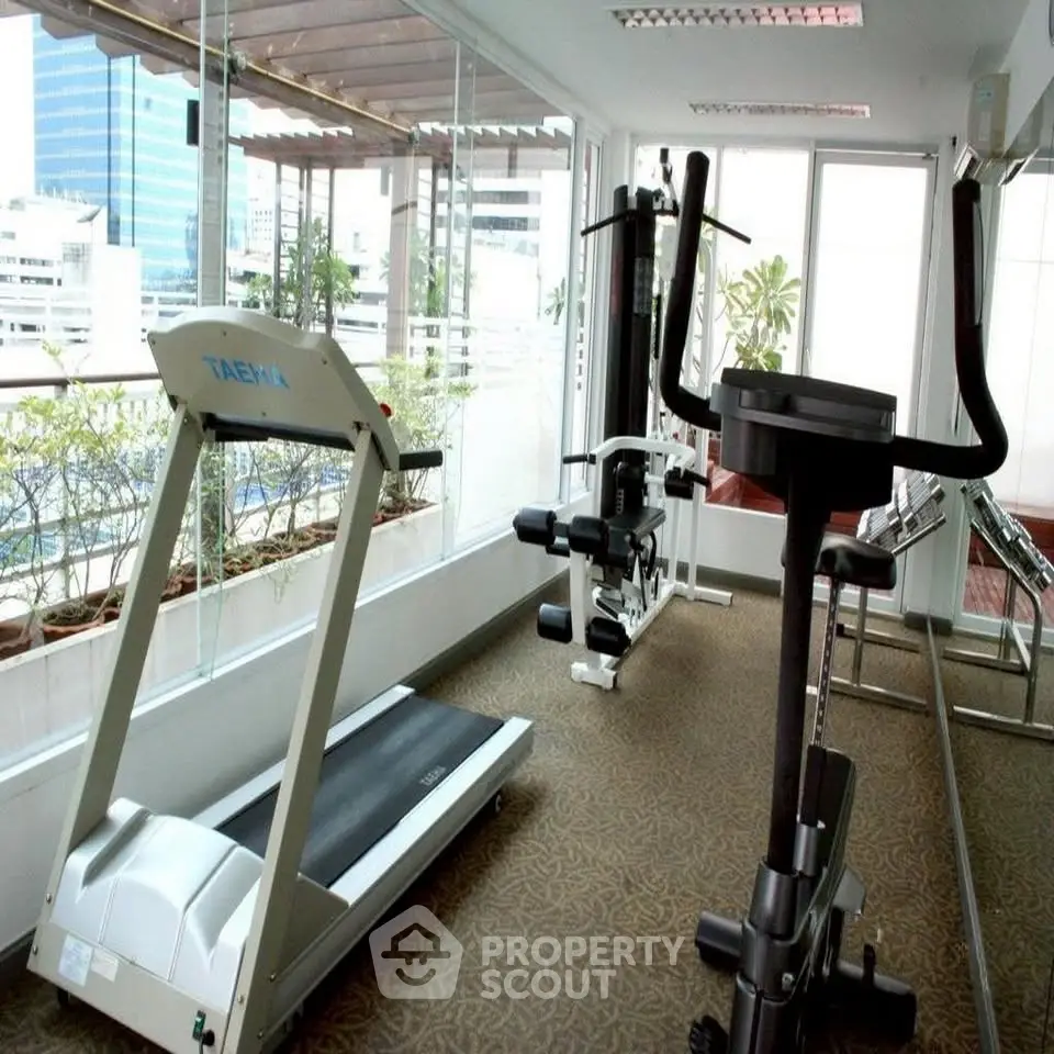 Modern gym with city view, featuring treadmill and exercise equipment in a bright, spacious area.