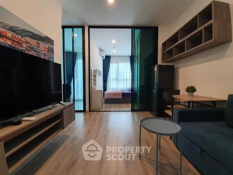 Modern living room with open view to bedroom, featuring sleek furniture and wooden flooring.