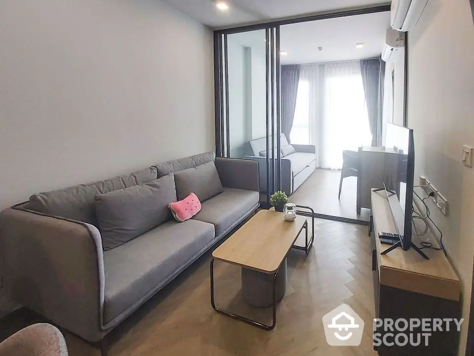 Modern living room with sleek grey sofa set, wooden coffee table, and natural light streaming from the balcony, perfect for urban living.