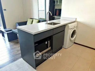 Modern kitchen with sleek island, built-in microwave, and washing machine in stylish apartment.