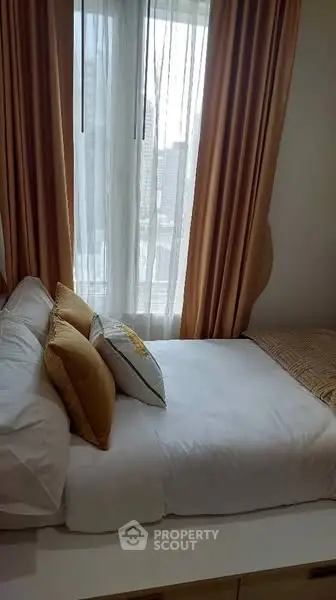 Cozy bedroom with plush pillows and city view through large window.