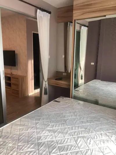 Modern bedroom with mirrored wardrobe and TV, featuring elegant decor and natural light.