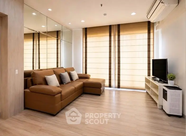 Modern living room with brown leather sofa, mirrored wall, and large windows with blinds.