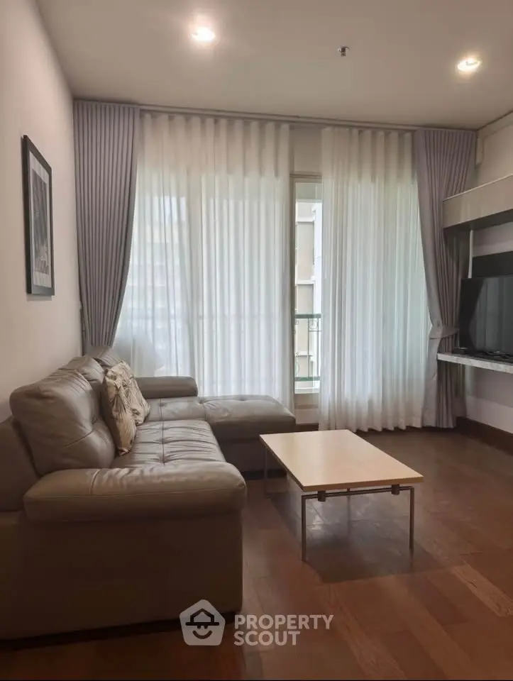 Modern living room with leather sofa, wooden floor, and large window with curtains.