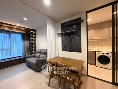 Modern living room with cozy seating and dining area, featuring a sleek washing machine in the open kitchen.