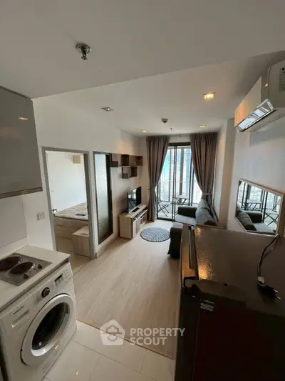 Modern apartment interior with open layout, featuring a cozy living room and compact kitchen with washing machine.