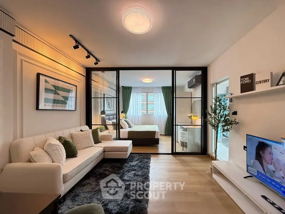 Modern living room with glass partition leading to a stylish bedroom, featuring elegant decor and ample natural light.