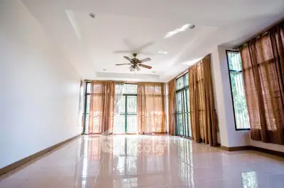 Spacious sunlit living room with large windows and ceiling fan
