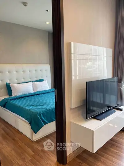 Modern bedroom with stylish decor and flat-screen TV, featuring elegant wood flooring and natural light.