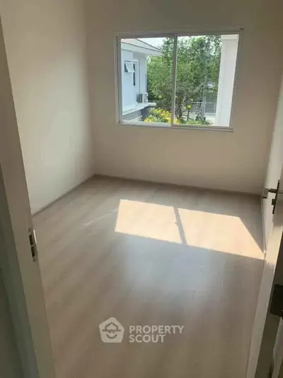 Bright empty bedroom with large window and wooden flooring