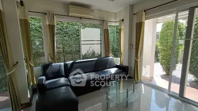 Spacious living room with large windows and garden view, featuring a modern black sofa and glass coffee table.
