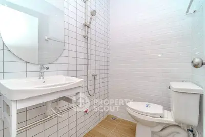 Modern bathroom with white tiles and sleek fixtures, featuring a shower and toilet.