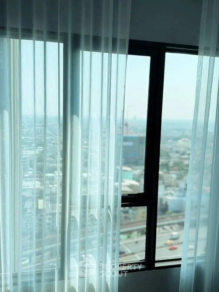Stunning cityscape view from a high-rise apartment window with sheer curtains.