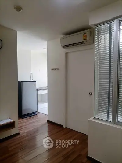 Modern apartment interior with wooden flooring and air conditioning, featuring a compact kitchen area.