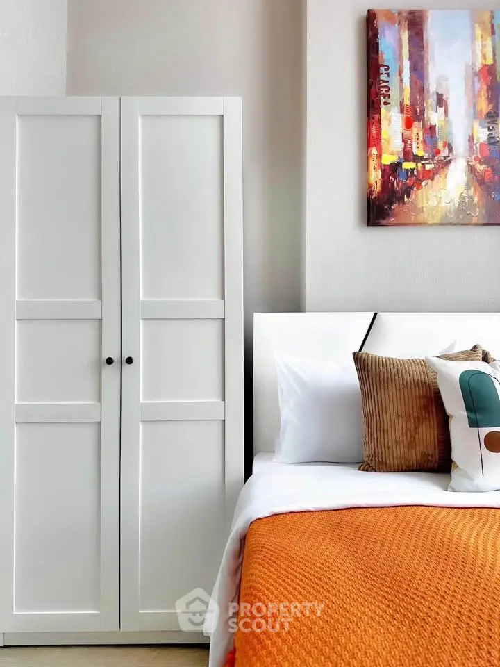 Modern bedroom with stylish decor and vibrant artwork, featuring a cozy bed and sleek wardrobe.